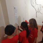 Three children touch the hands on tactile display next to the Wire Sculpture it is based on.