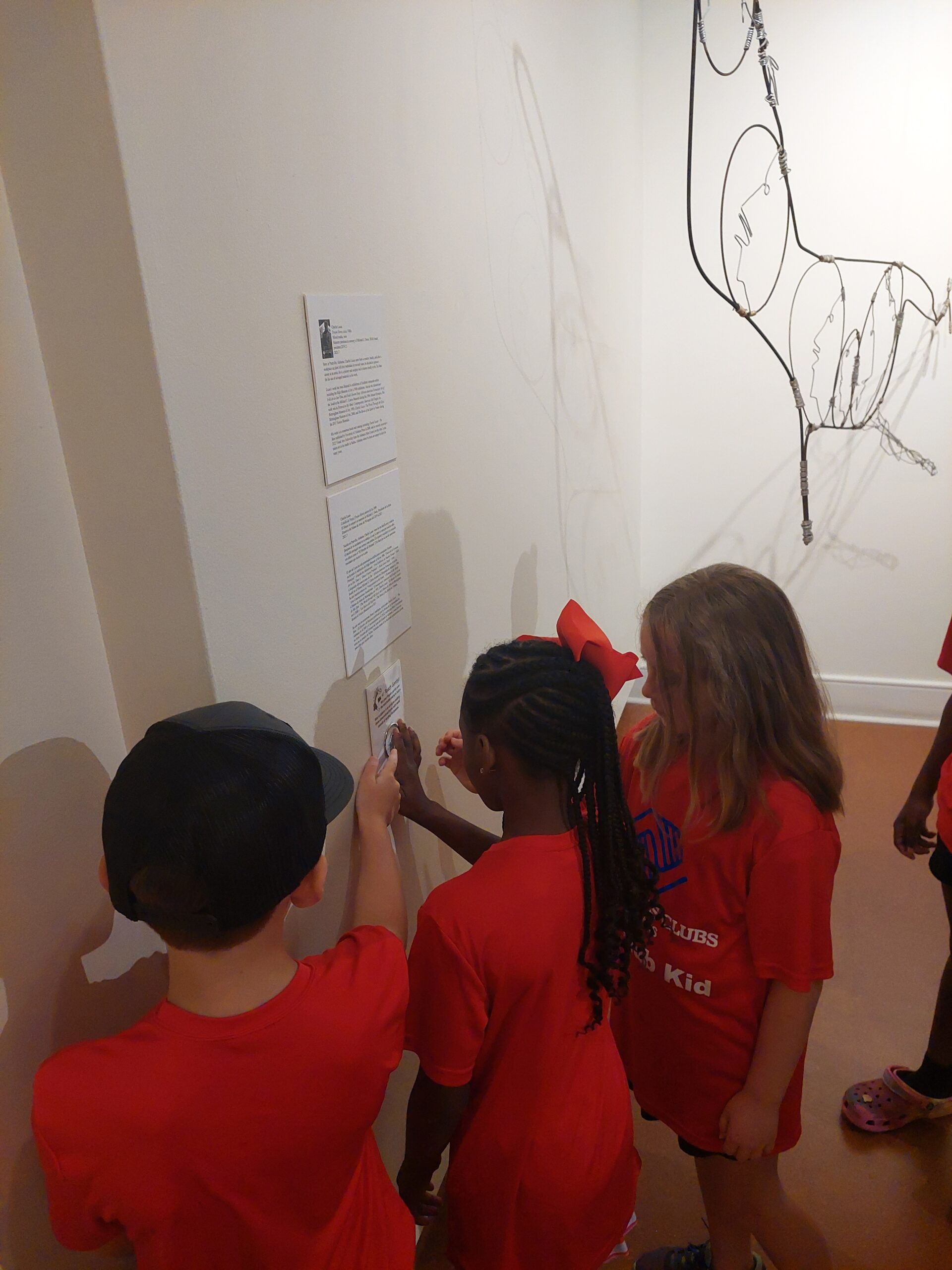 Three children touch the hands on tactile display next to the Wire Sculpture it is based on.