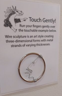 Irwin, the museum dragon, on a "Touch Gently!" tactile sample of wire sculpture.